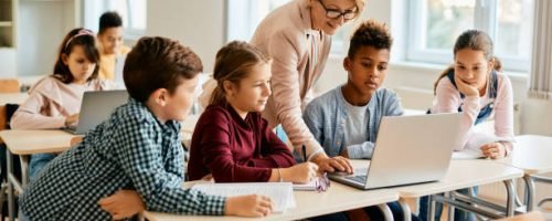 Elementary teacher and her students using laptop during computer class at school.